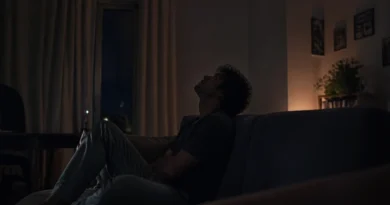 Young person sitting alone on a couch at night, looking upward in a dimly lit room, reflecting silently